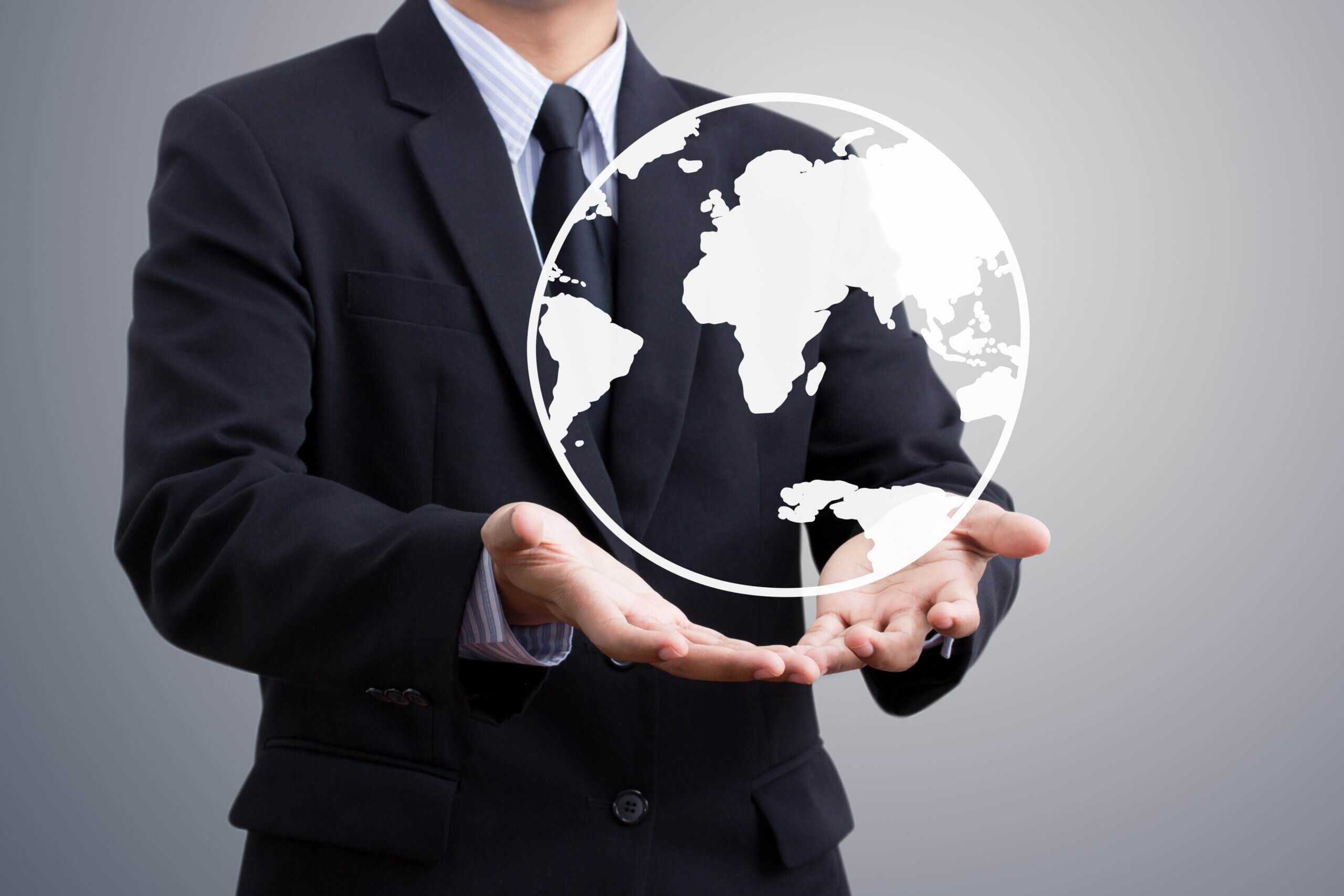 A person in a suit holds their hands out, palms up, with a transparent globe graphic floating above, showing a simplified world map. The background is a plain, light gradient.