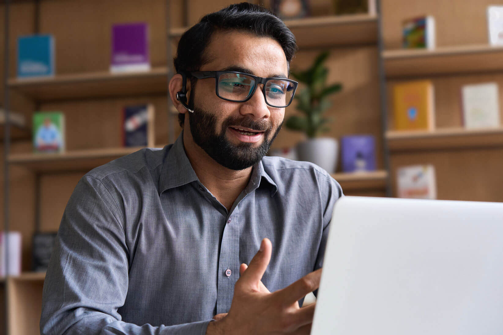 A person wearing glasses and a headset is sitting in front of a laptop, gesturing with one hand during a video call or online meeting, representing Cogency Global’s ability to act as a Duly Authorized Representative in all US jurisdictions.