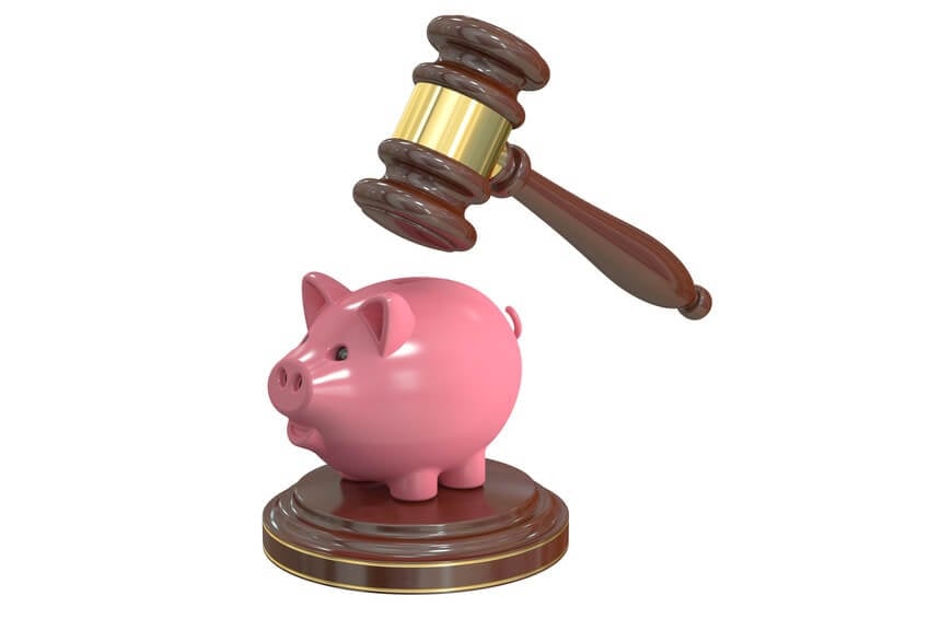 A wooden gavel is hovering above a pink piggy bank standing on a round wooden base. The image suggests themes of financial decisions, legal actions, or savings. The background is white.