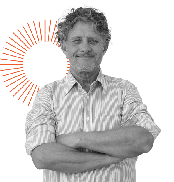 A man with curly hair and a beard smiles while standing with arms crossed. He is wearing a striped shirt. A black circle and a red starburst design are in the background.