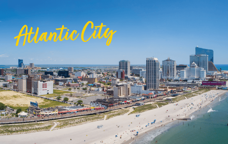Aerial view of Atlantic City’s beach and boardwalk with tall buildings and casinos under a clear blue sky. “Atlantic City” is written in bright yellow script in the top left corner, highlighting the site of upcoming lending conferences 2025.