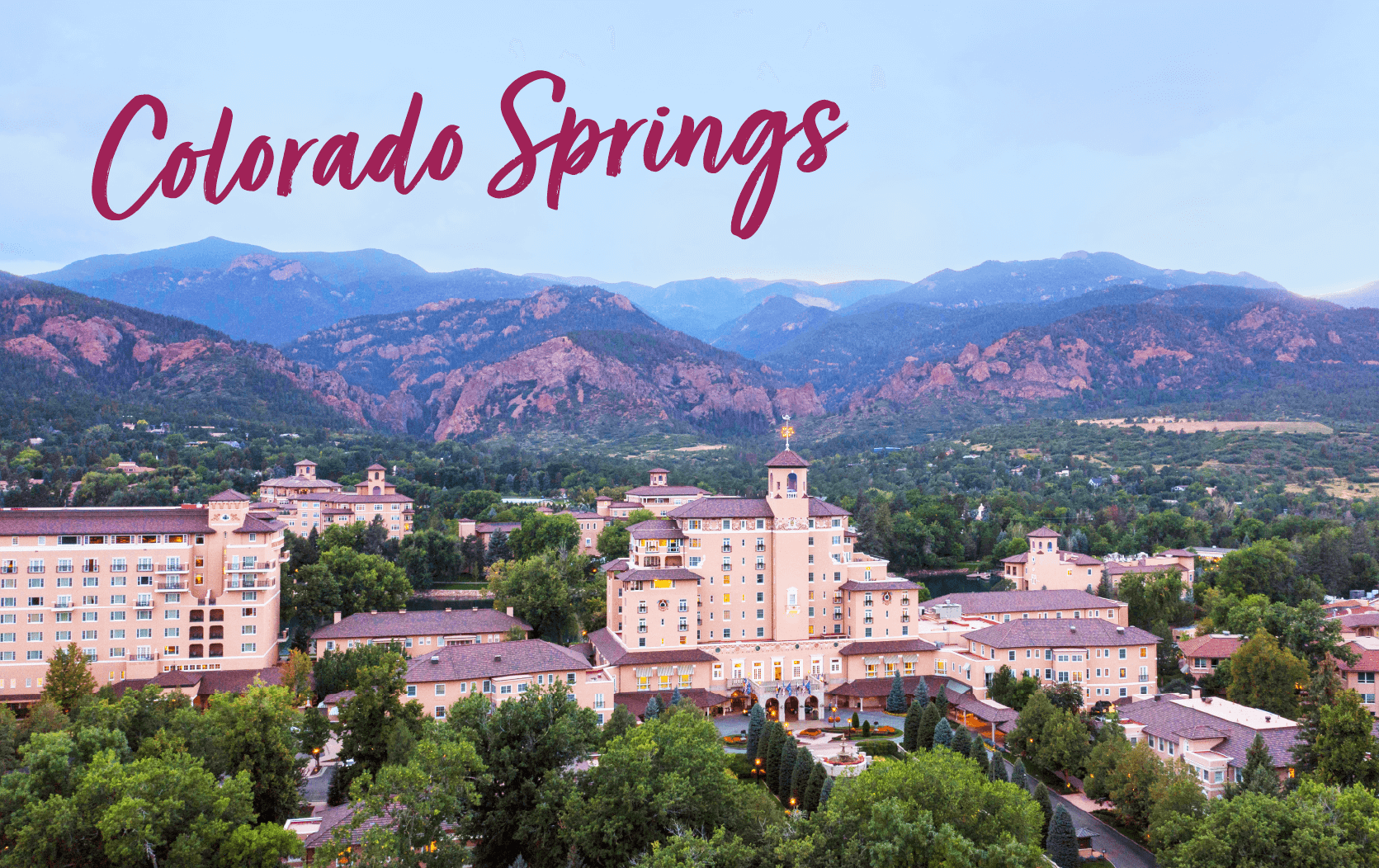 Aerial view of a large resort complex surrounded by trees and mountains, with "Colorado Springs" in bold script across the sky—an ideal setting for upcoming lending conferences 2025.