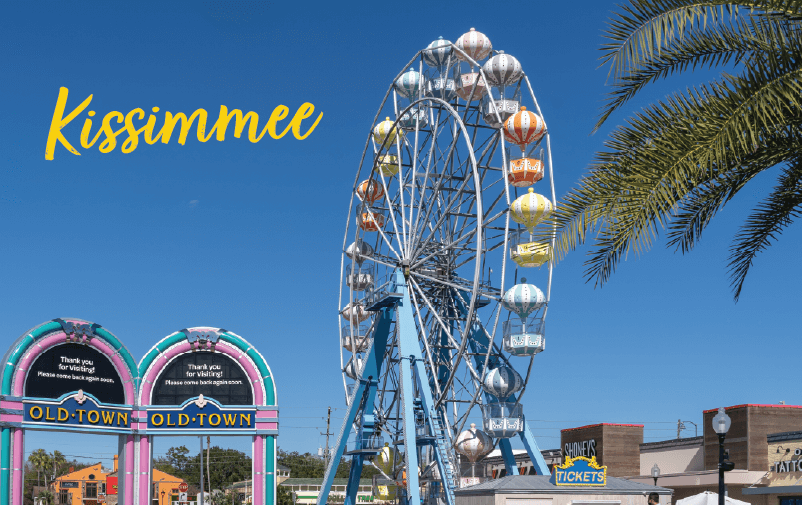 A Ferris wheel with colorful gondolas stands against a clear blue sky in Old Town, Kissimmee. Palm trees and ticket booths are nearby, with “Kissimmee” in yellow script—a vibrant spot perfect for lending conferences 2025.