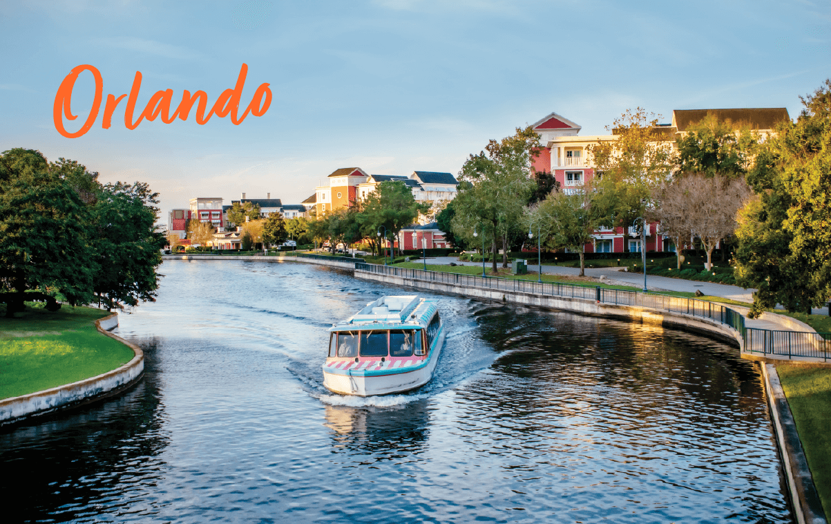 A boat cruises along a peaceful canal lined with trees and colorful buildings in Orlando, Florida, under a clear blue sky—an inviting scene for the upcoming lending conferences 2025. The word "Orlando" is written in orange text in the top left corner.