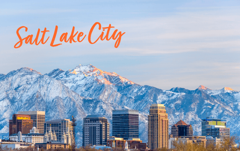 Salt Lake City skyline with modern buildings in front of snow-covered mountains under a blue sky; "Salt Lake City" is written in orange script at the top left, making it an ideal setting for lending conferences 2025.